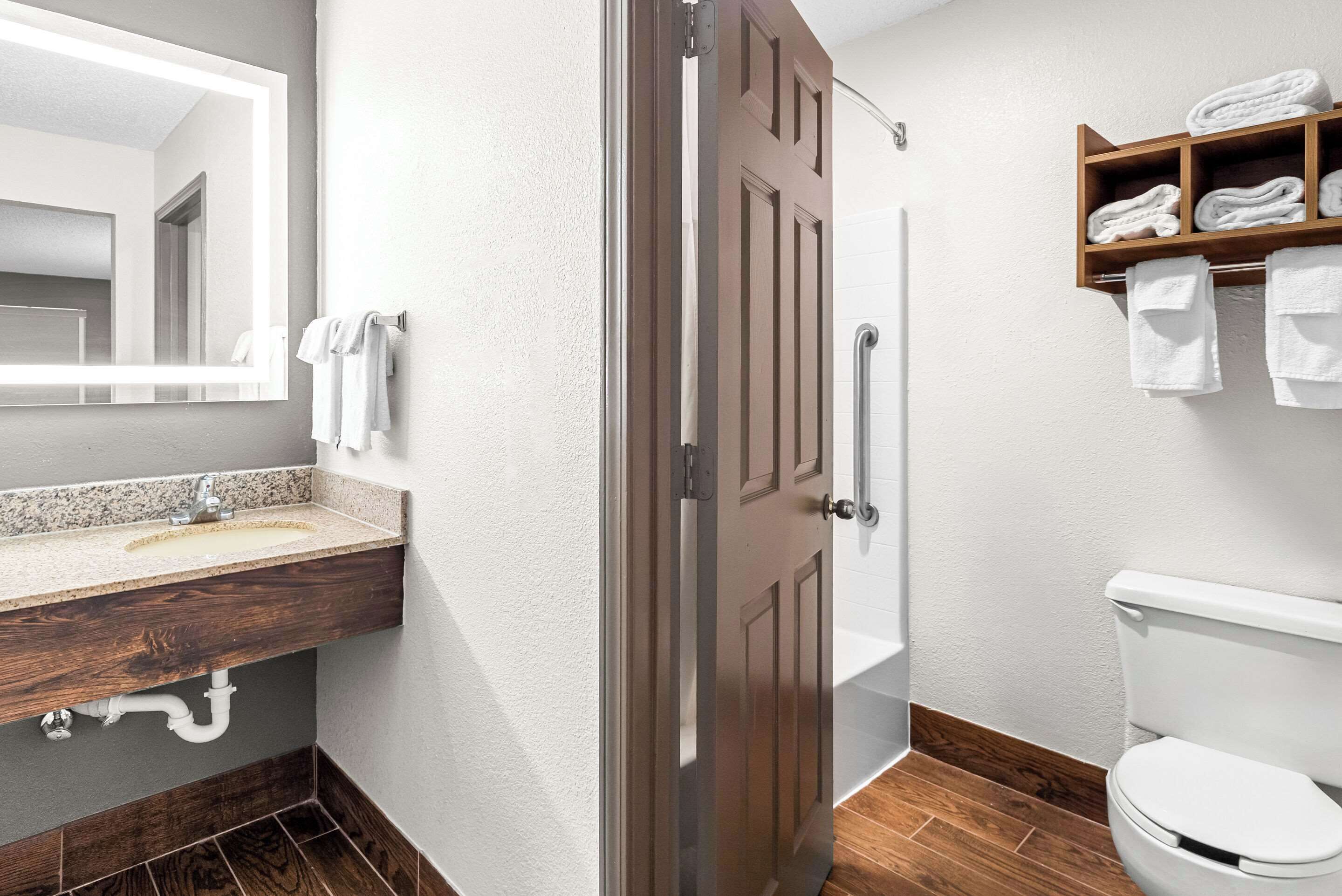 A bathroom with a wooden vanity, a sink, a mirror, a toilet, and a shelf with towels.