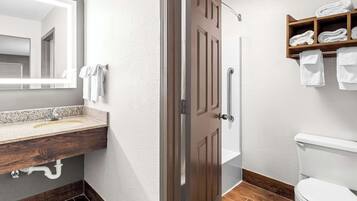 A bathroom with a wooden vanity, a sink, a mirror, a toilet, and a shelf with towels.