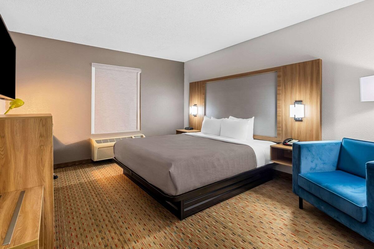A hotel room with a bed, a desk, a chair, and a large window.