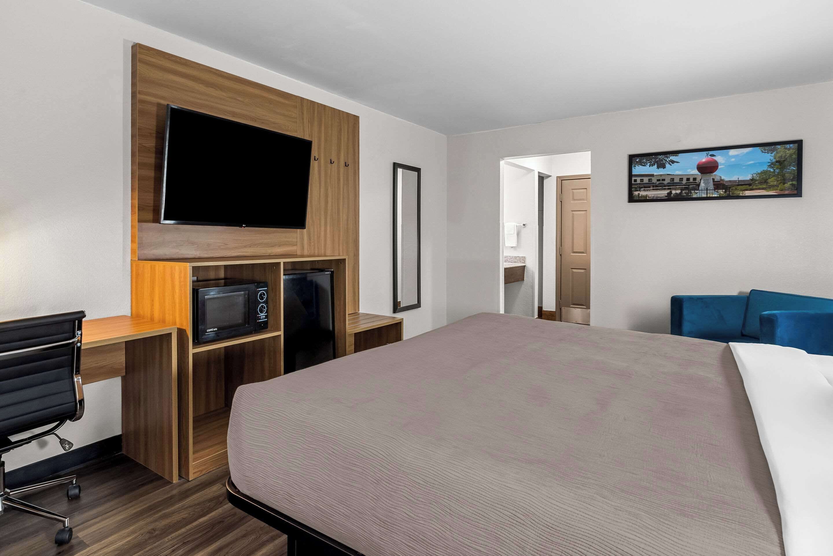 A hotel room with a bed, a desk with a TV, a microwave, and a chair.