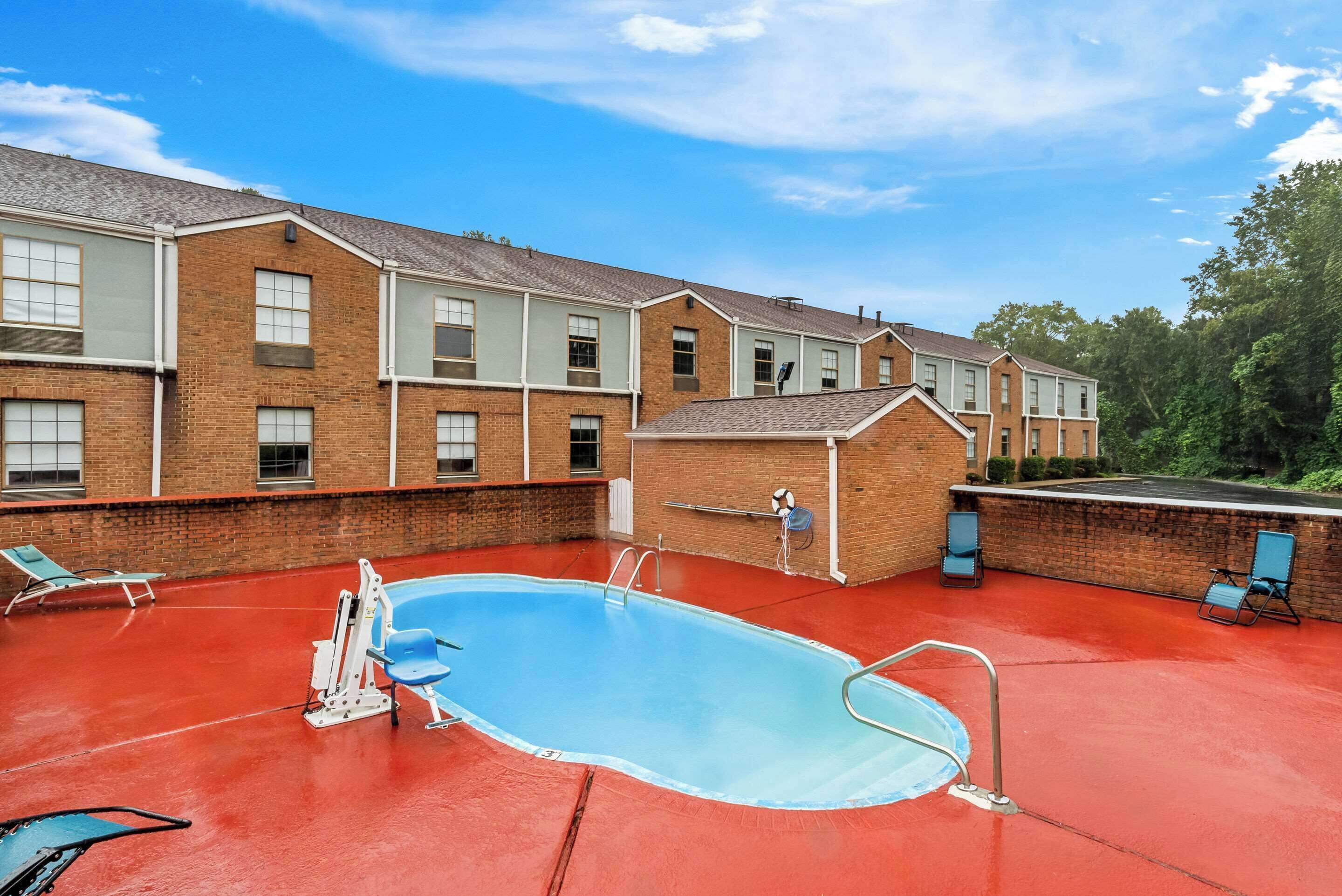 A swimming pool with a red deck, surrounded by a brick building with multiple windows and a flat roof.