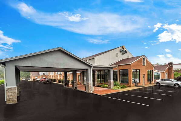 A hotel with a covered parking area, a brick building, and a clear blue sky.