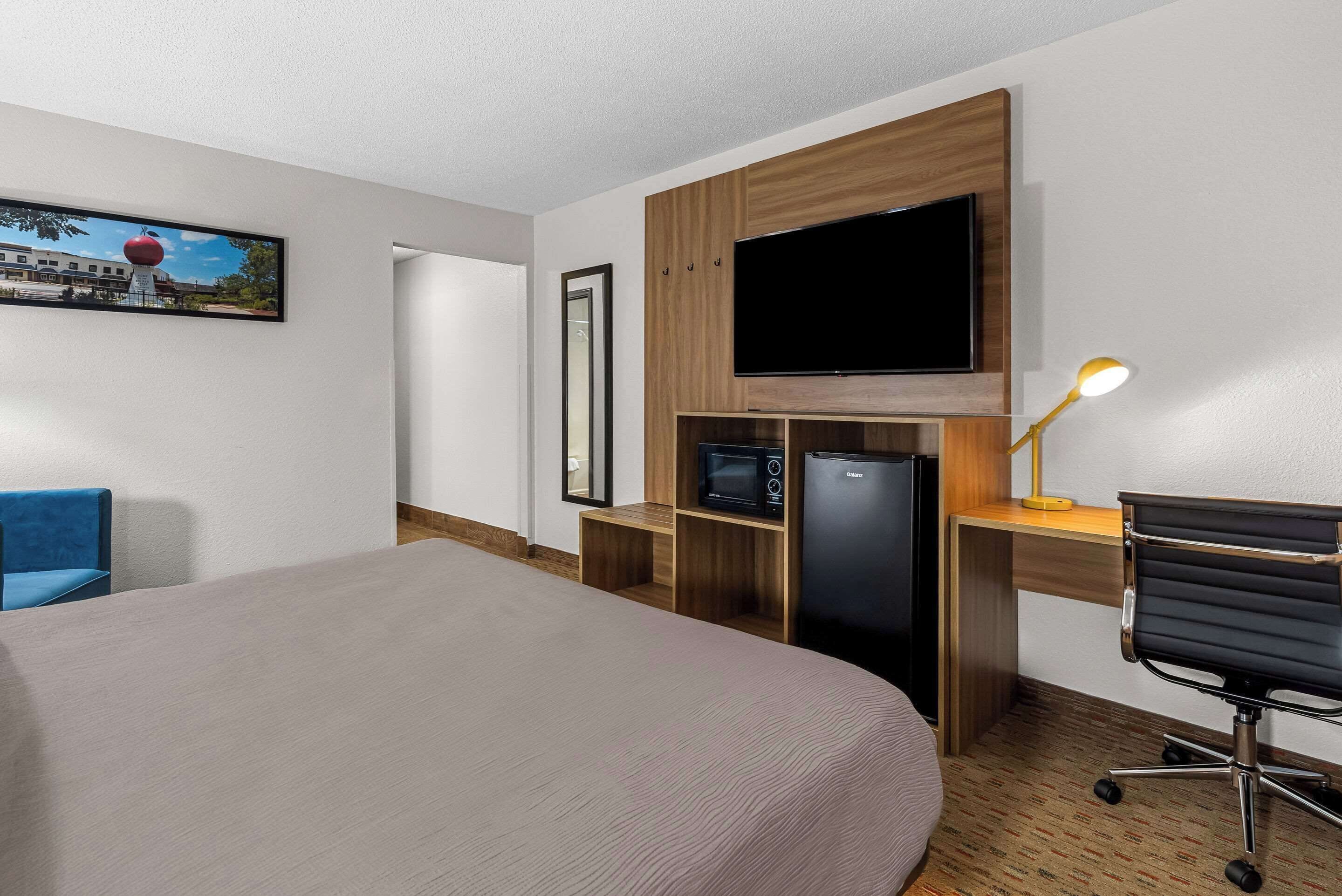 Habitación de hotel con cama, escritorio con computadora, televisor, microondas y refrigerador.