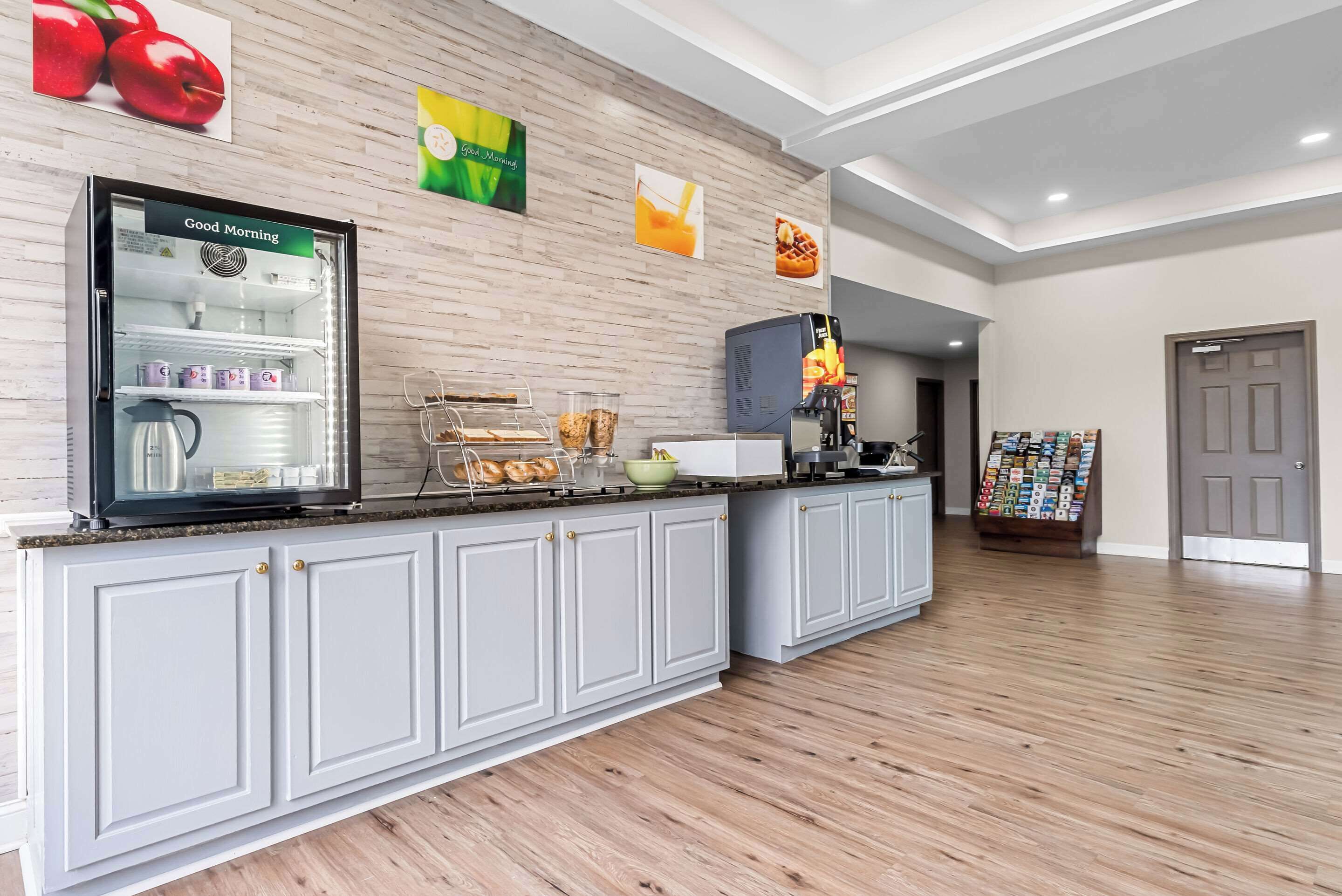 Eine moderne Hotelhalle mit Frühstücksbar, einem Kühlschrank mit der Aufschrift 'Guten Morgen' und einer Kaffeemaschine.