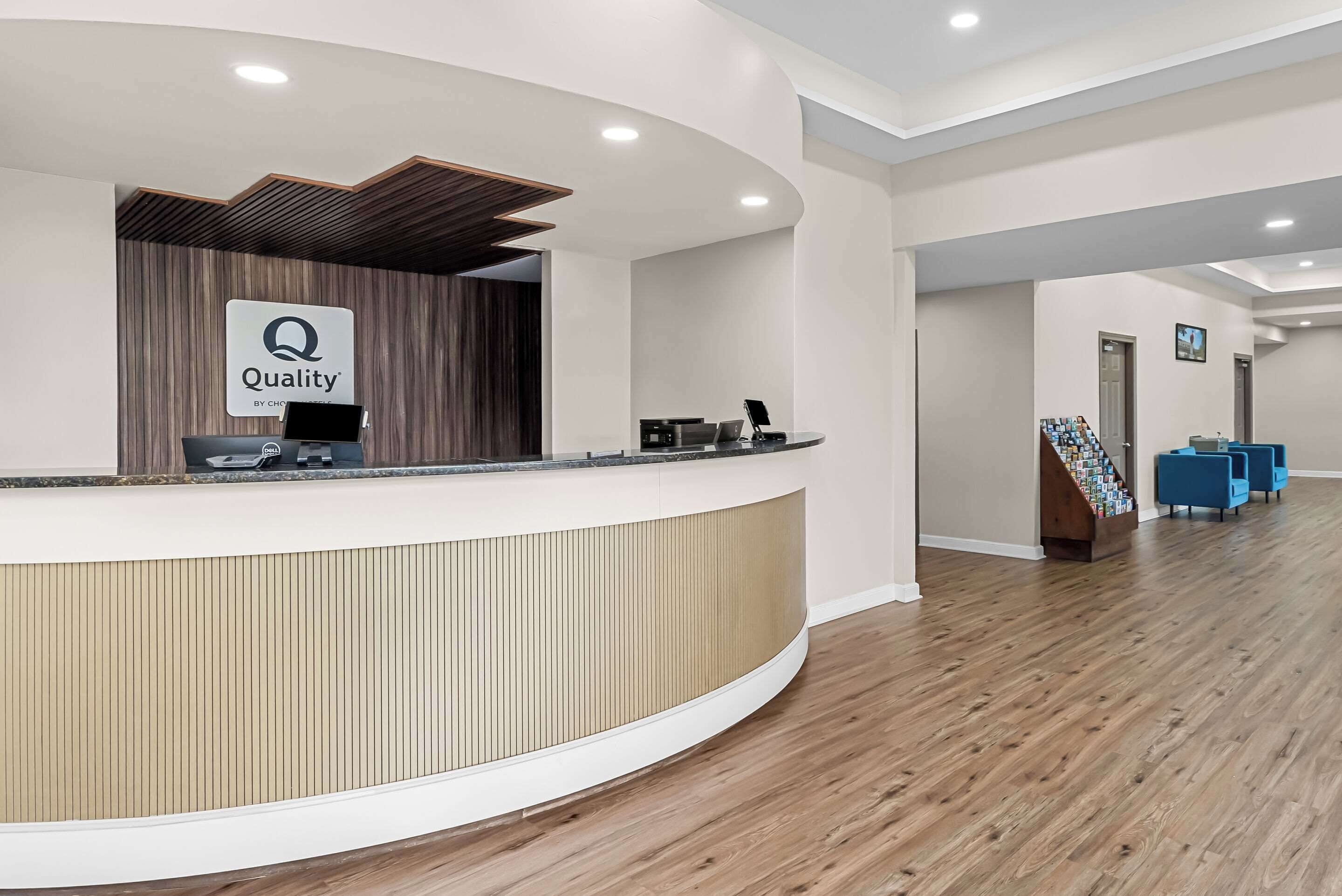 Una zona d'entrada moderna amb un taulell de recepció corbat, un senyal amb la paraula 'Quality', un ordinador portàtil i un arxivador de revistes.