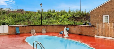 A swimming pool with a red deck, surrounded by a brick wall and a wooden fence.