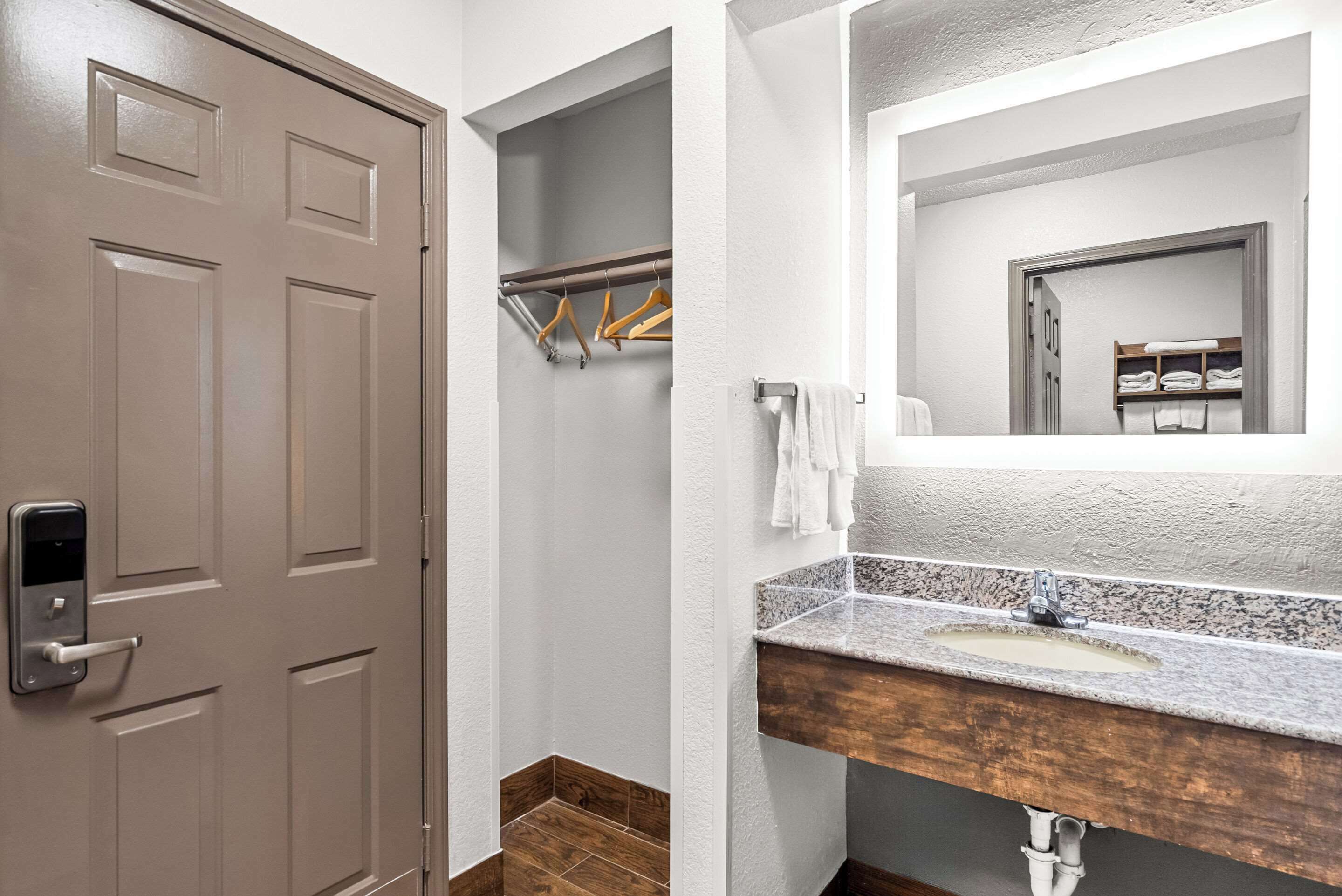 A bathroom with a wooden door, a towel rack, and a sink with a granite countertop.