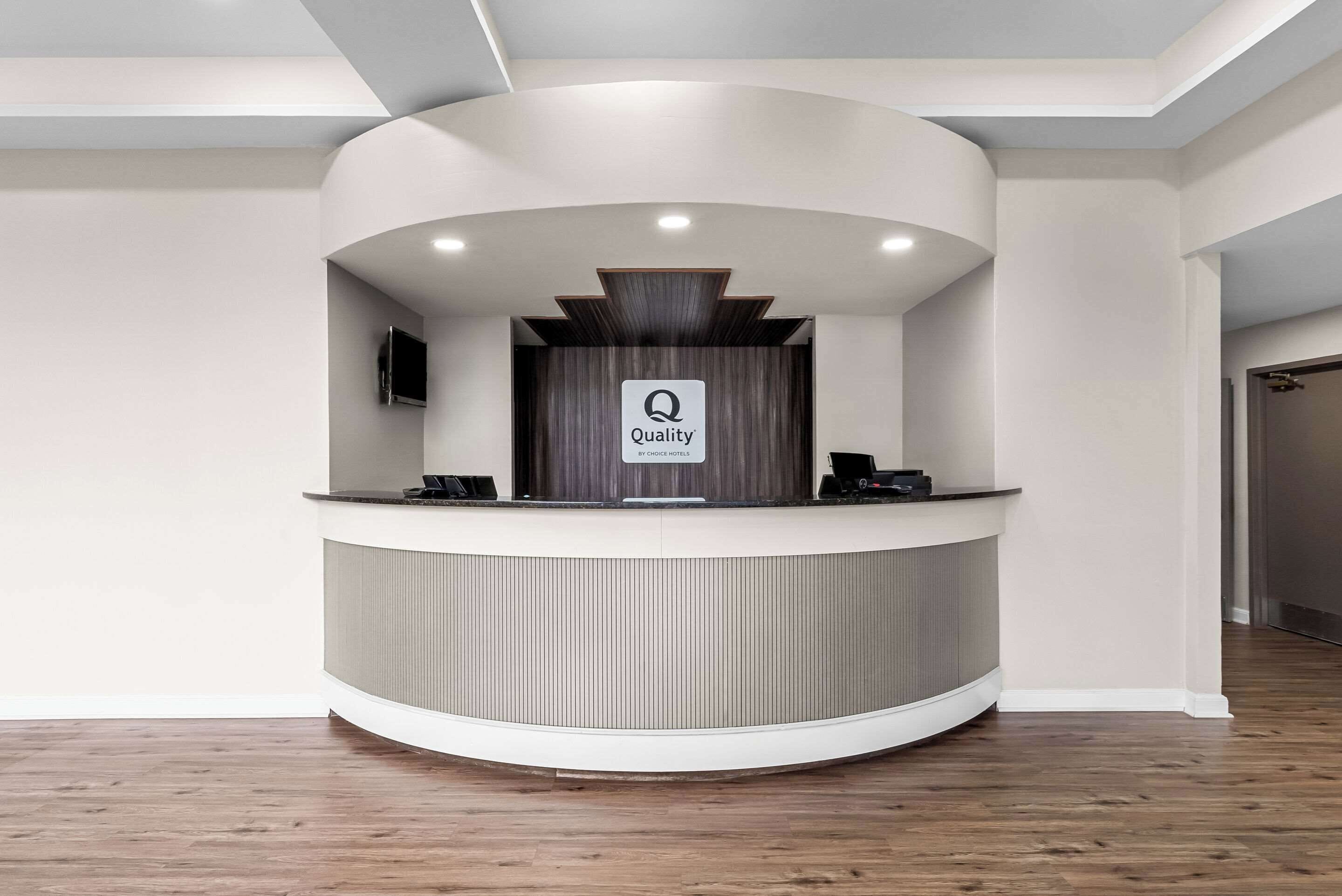 Een hotel receptiebalie met een 'Quality by Choice Hotels' bord, een flatscreen televisie en een telefoon.