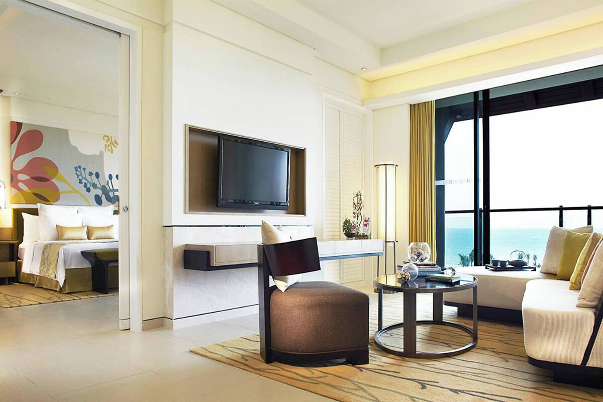 A modern hotel room with a bed, a sofa, a TV, and a balcony with a view of the ocean.