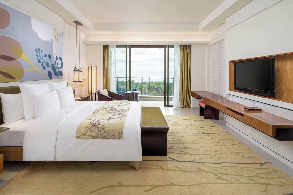 A hotel room with a large bed, a television, a desk, and a view of the outdoors.