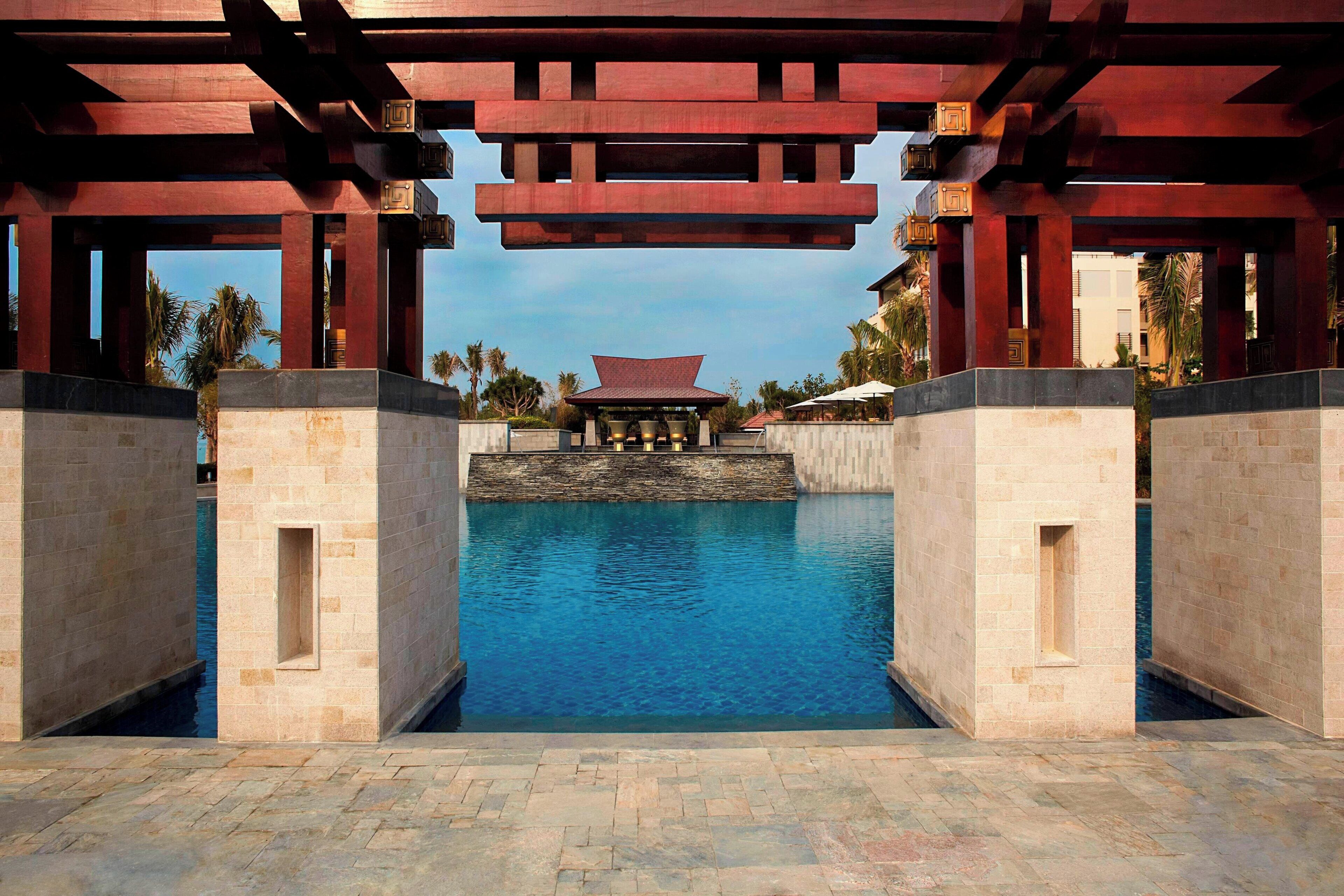 A pool area with a traditional architectural structure overhead, stone walls, and a clear view of the pool.