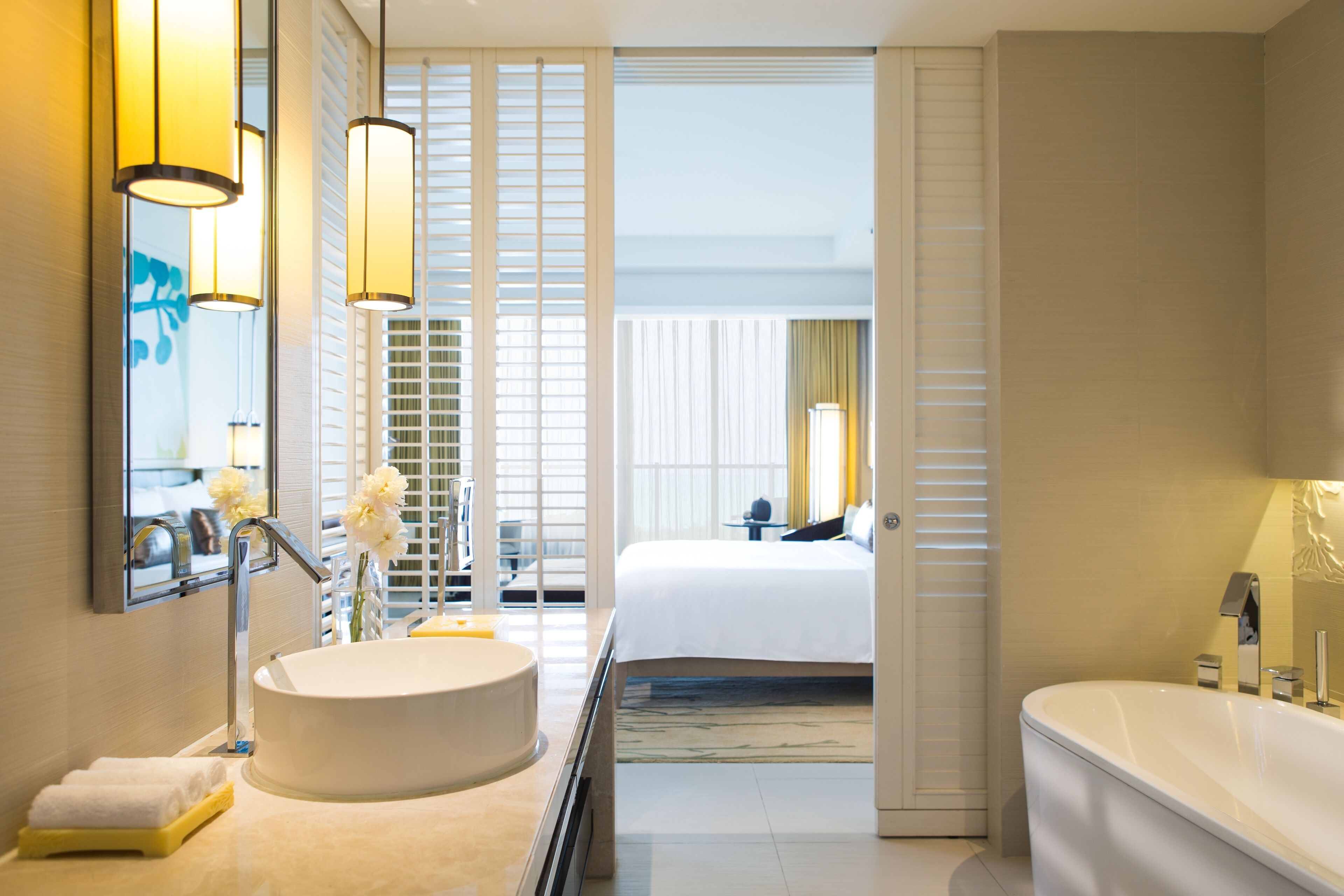 Een moderne hotelbadkamer met een groot wastafel, een bad en een bed dat door een open deur zichtbaar is.
