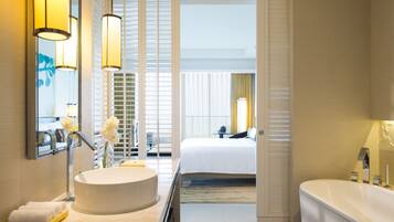 Een moderne hotelbadkamer met een groot wastafel, een bad en een bed dat door een open deur zichtbaar is.