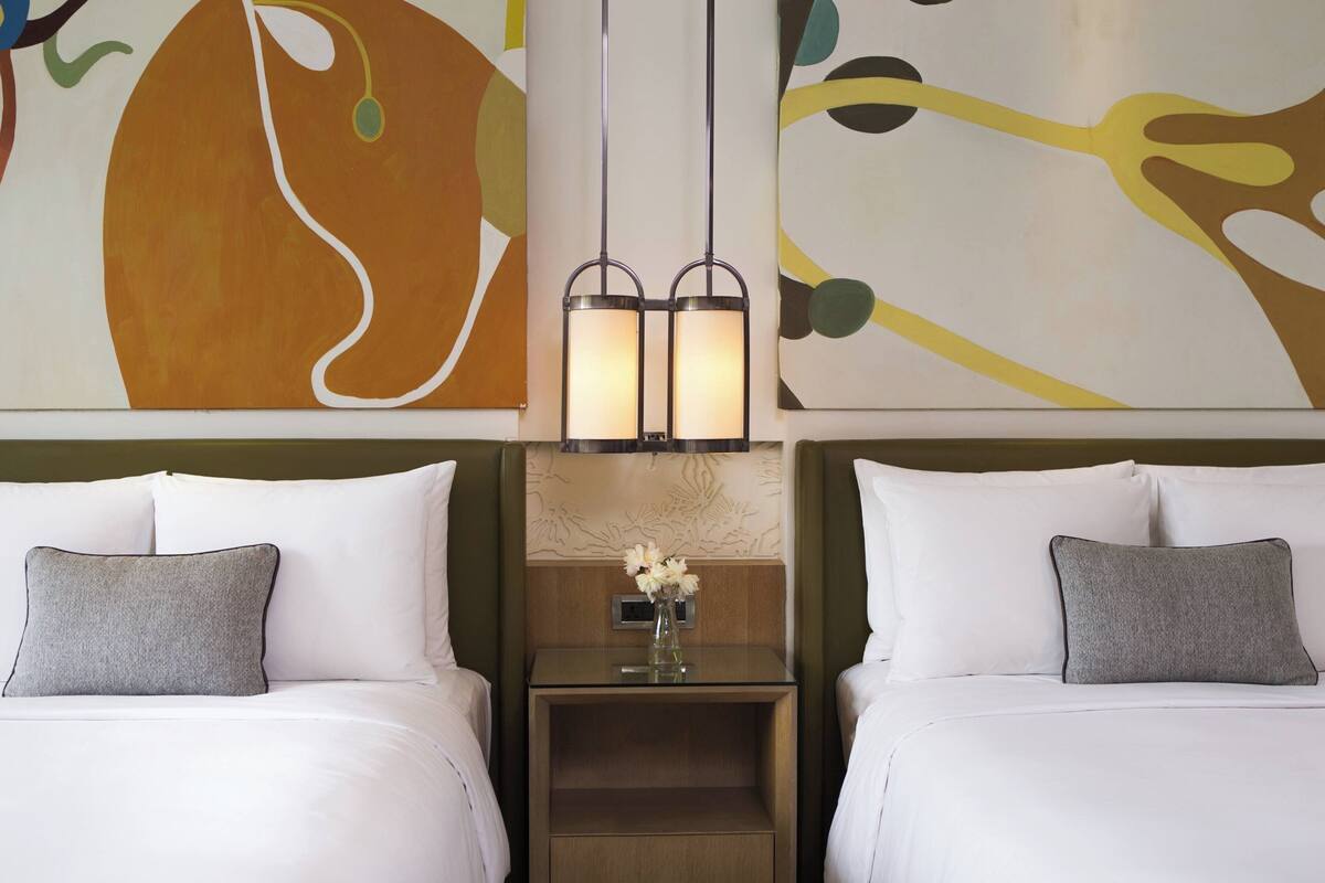 A hotel room with two beds, a nightstand with a vase of flowers, and abstract wall art.