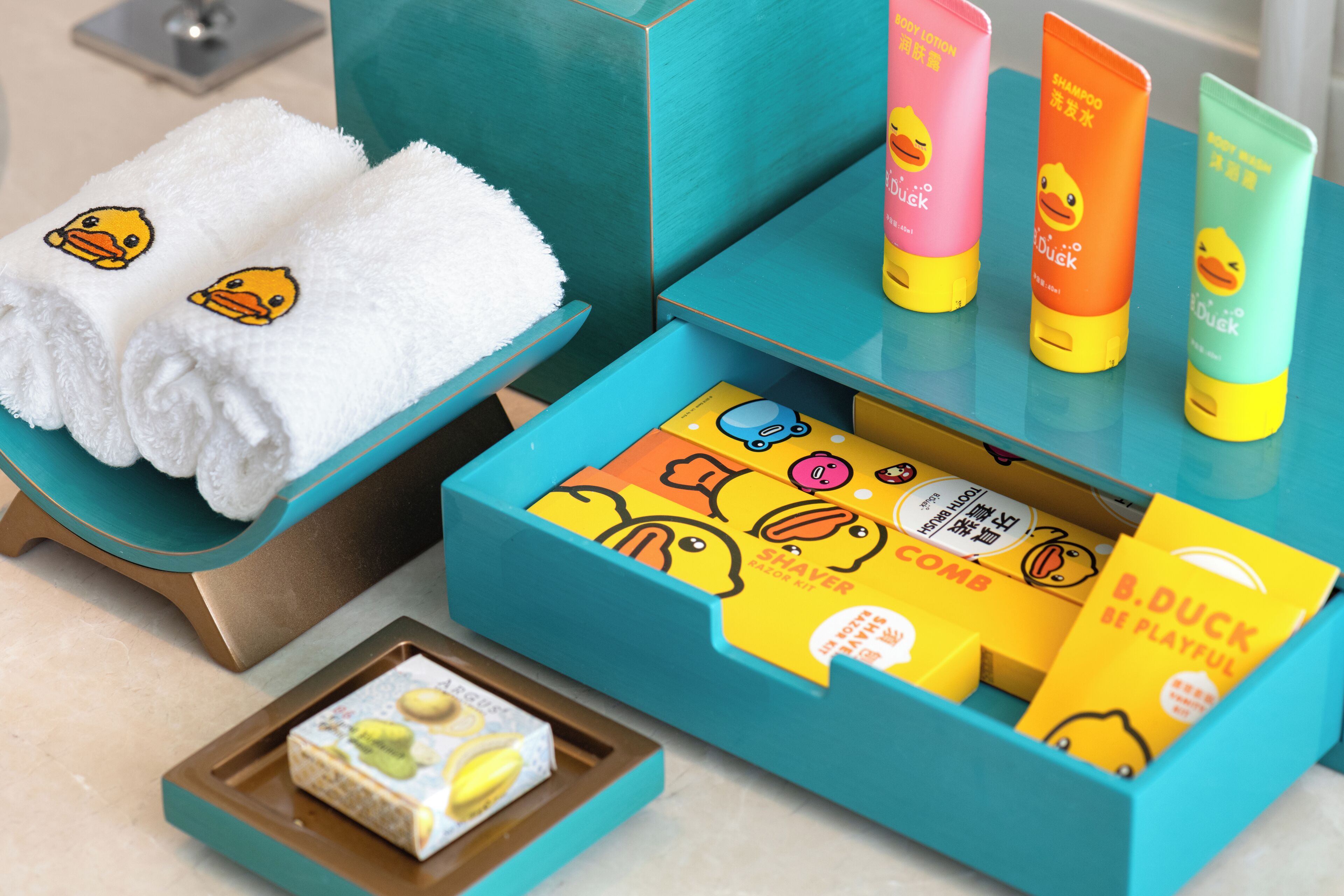 A bathroom with a teal vanity, white towels with duck designs, and various toiletries including a toothbrush and toothpaste.