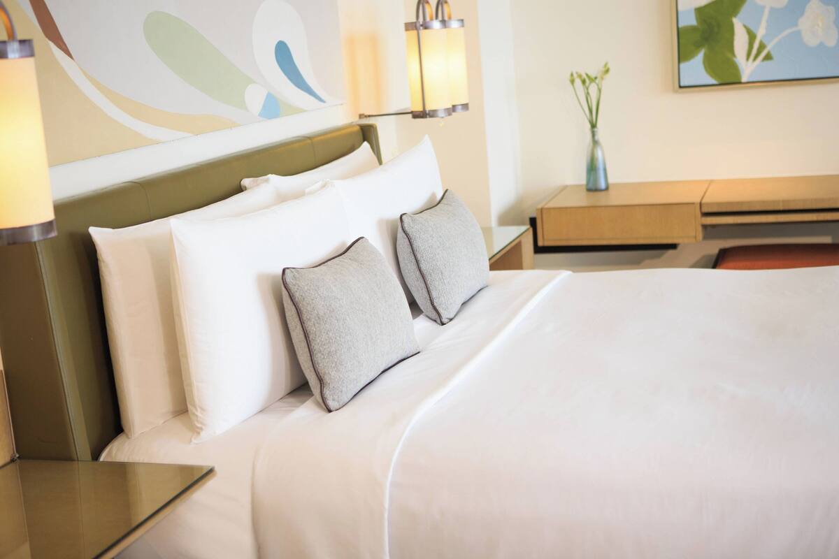 A hotel room with a neatly made bed, a bedside table, a lamp, and a vase with flowers on a nightstand.