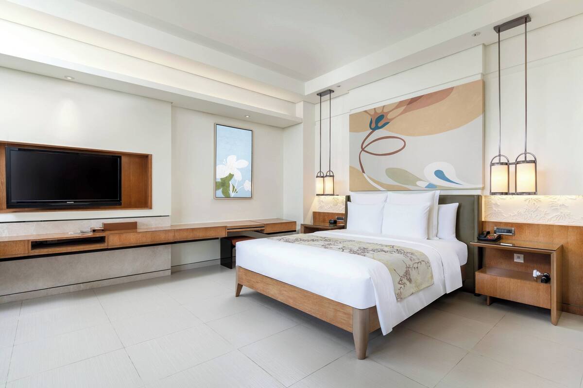 A modern hotel room with a large bed, a flat-screen TV, a desk, and a nightstand.