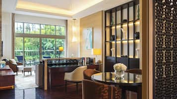 Una habitación de hotel moderna con zona de comedor, bar y ventanas amplias con vistas a zonas verdes.