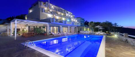 A modern two-story building with a swimming pool, outdoor seating, and a covered patio area.