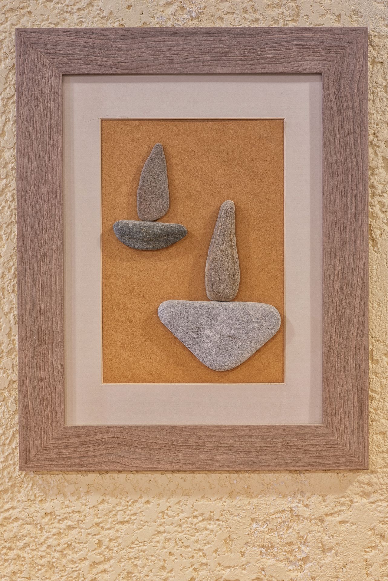 A framed artwork with three stone shapes on a textured wall.
