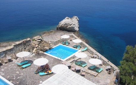 A pool area with lounge chairs and umbrellas, overlooking a clear blue sea.
