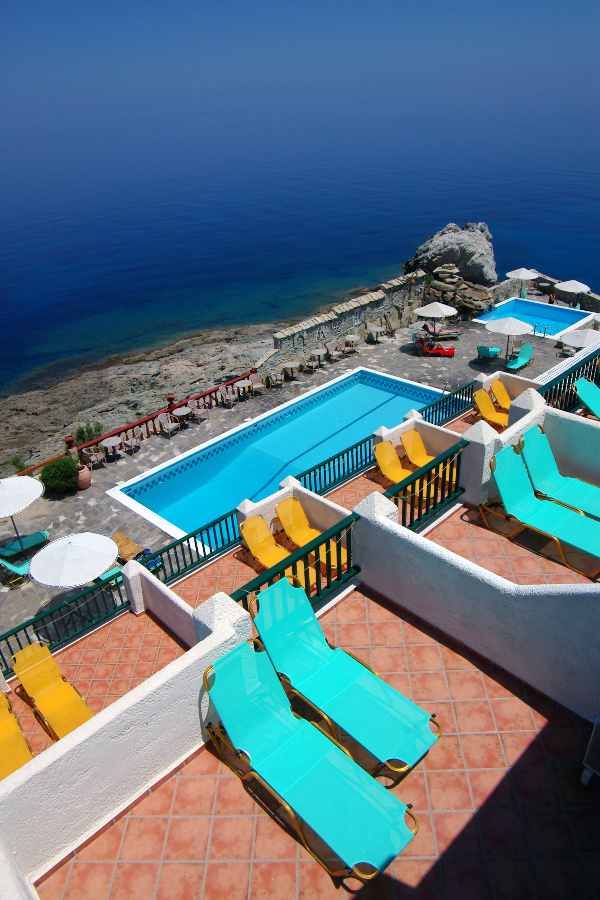 A rooftop pool area with multiple sun loungers and umbrellas, overlooking a beach and the sea.