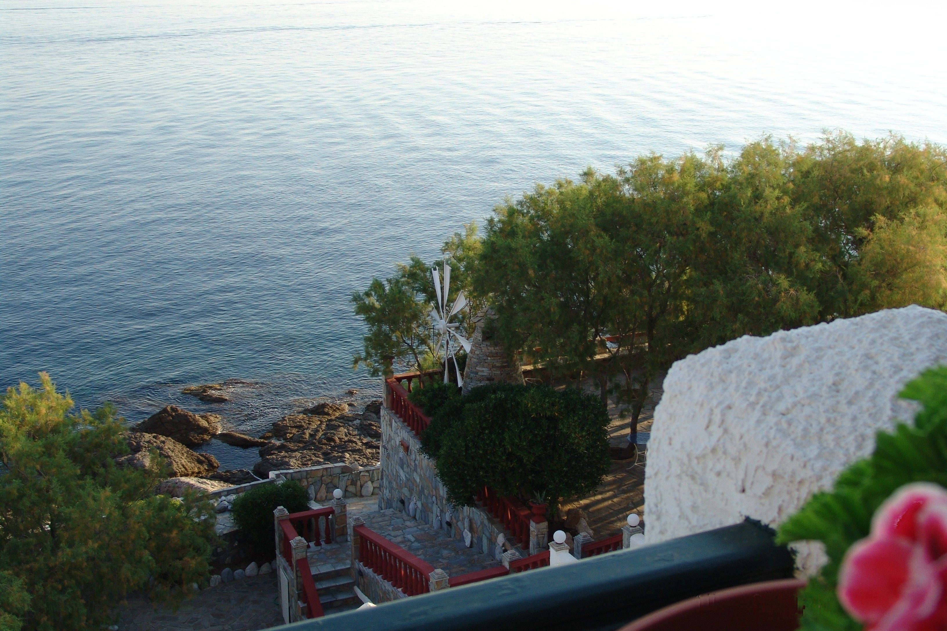 A coastal view with a stone staircase leading down to the beach, surrounded by trees and a white building.