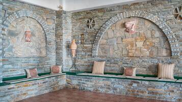 A stone-walled room with a fireplace, green cushioned seating, and decorative pottery.