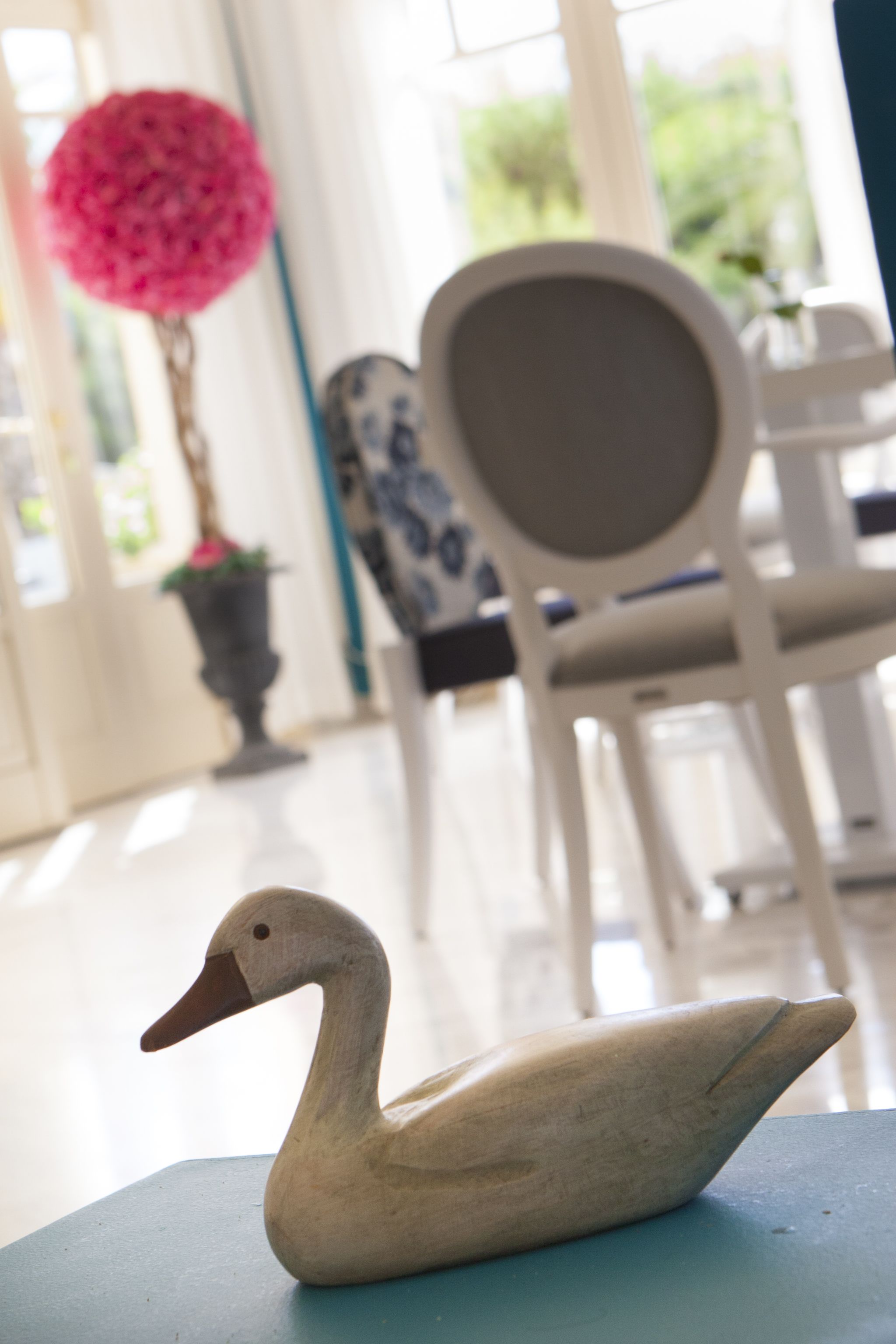 Una escultura de cisne sobre una mesa en una habitación con una silla y una planta en maceta al fondo.