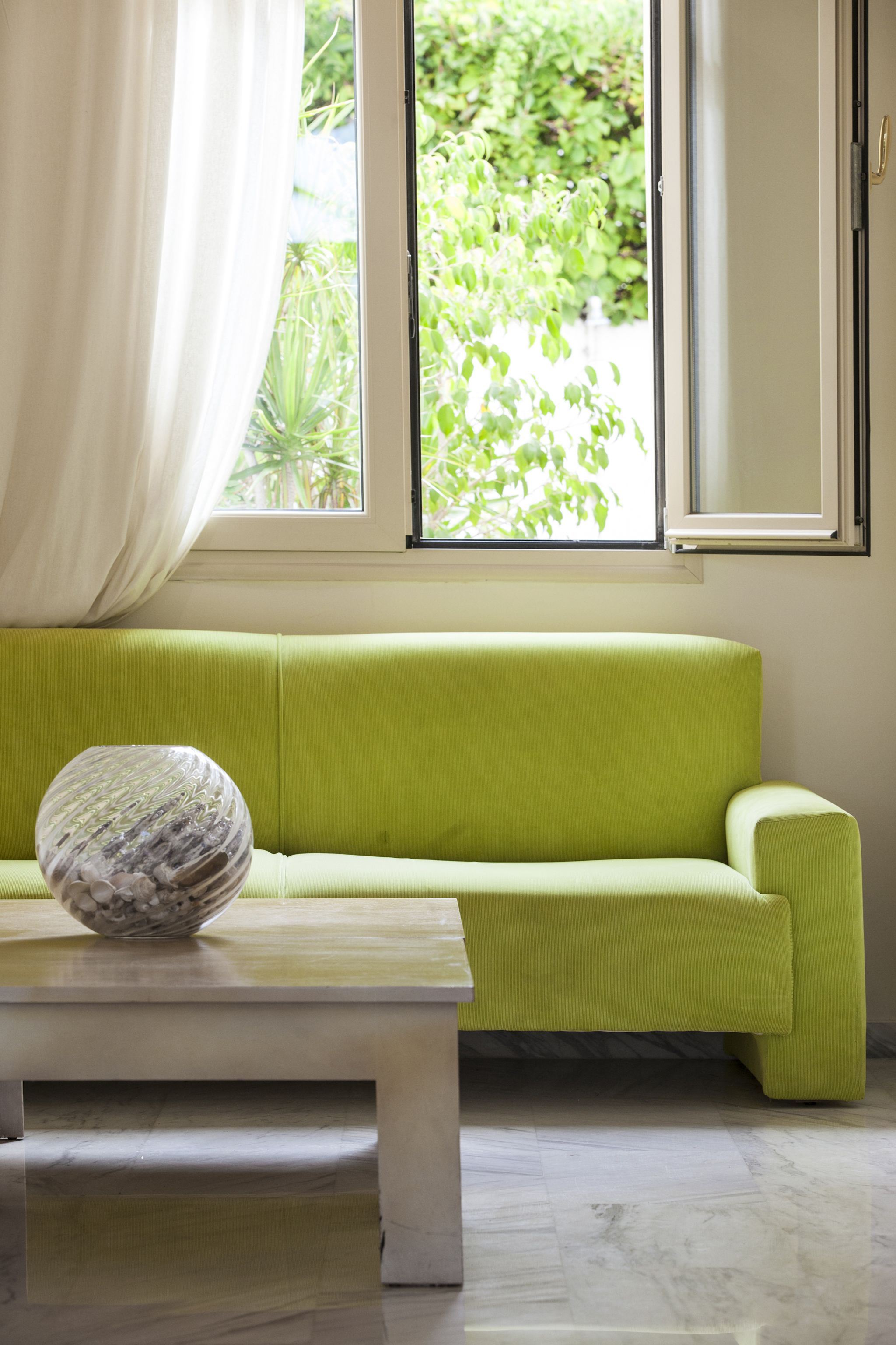 A room with a green sofa, a white coffee table, and a window with curtains.