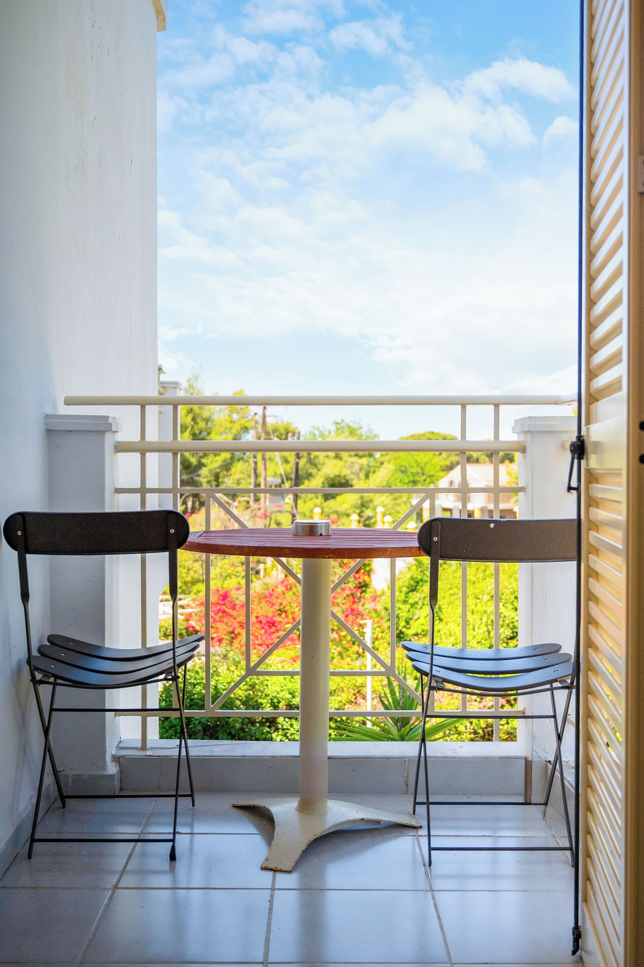 Un balcon avec deux chaises et une table, offrant une vue sur la verdure et un ciel dégagé.