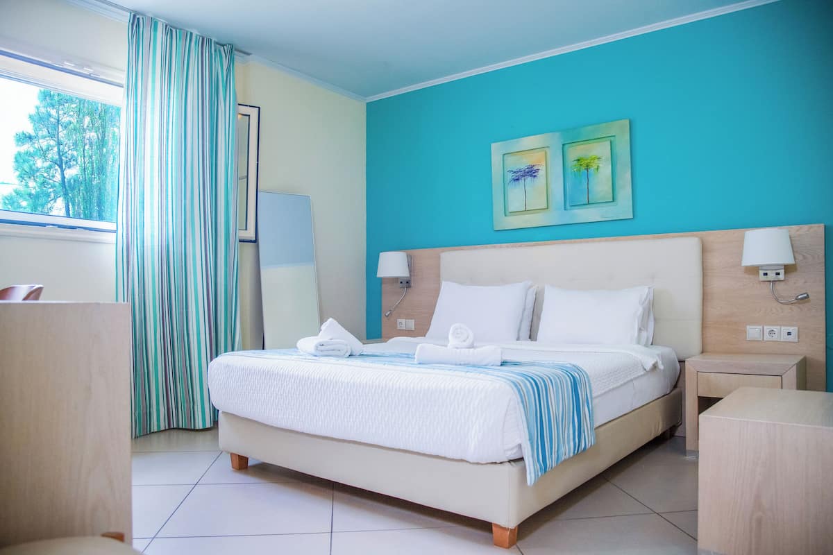 A hotel room with a bed, bedside tables, a window with curtains, and artwork on the wall.