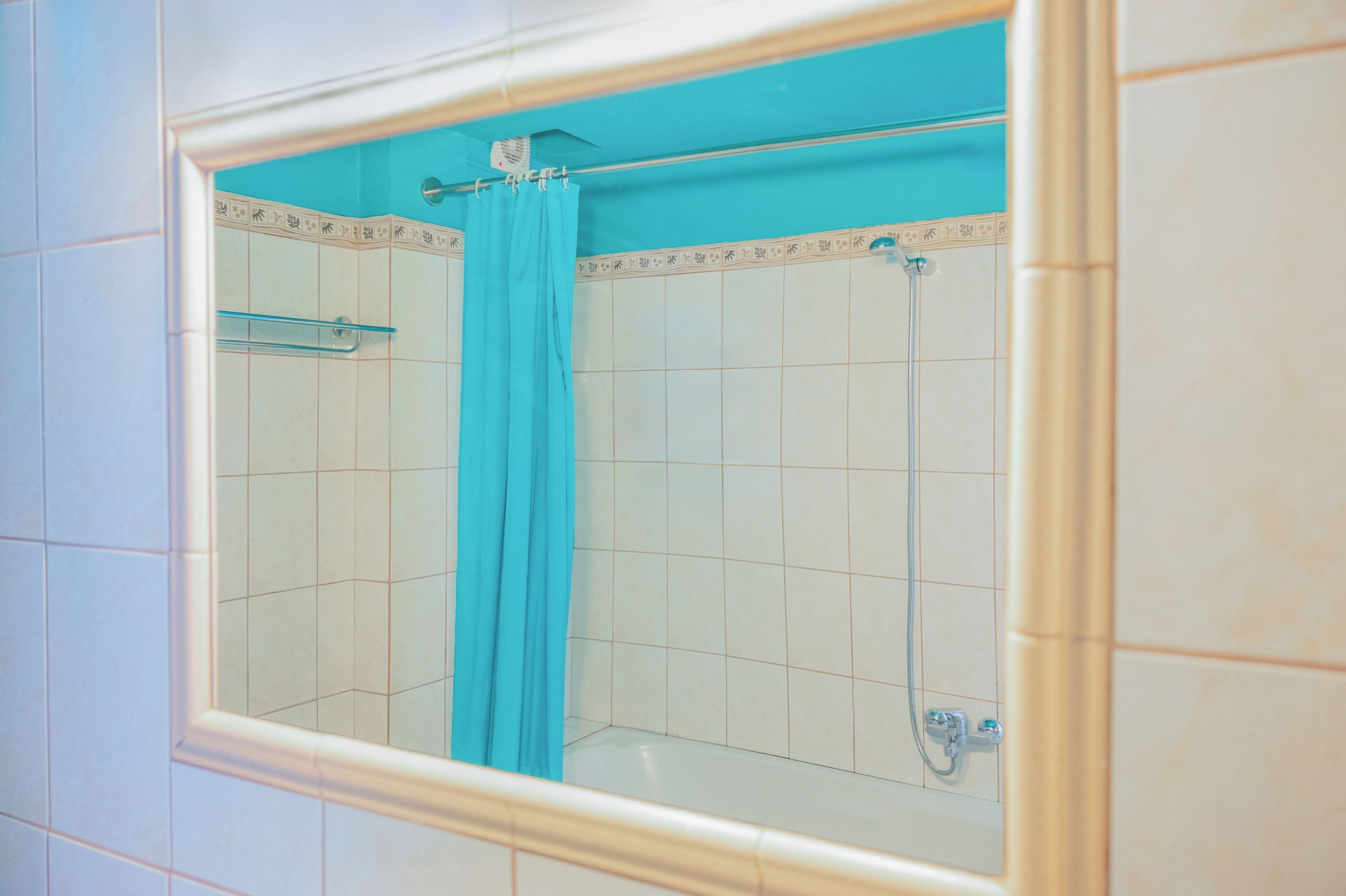 Un baño con ducha, estante de vidrio y cortina azul.