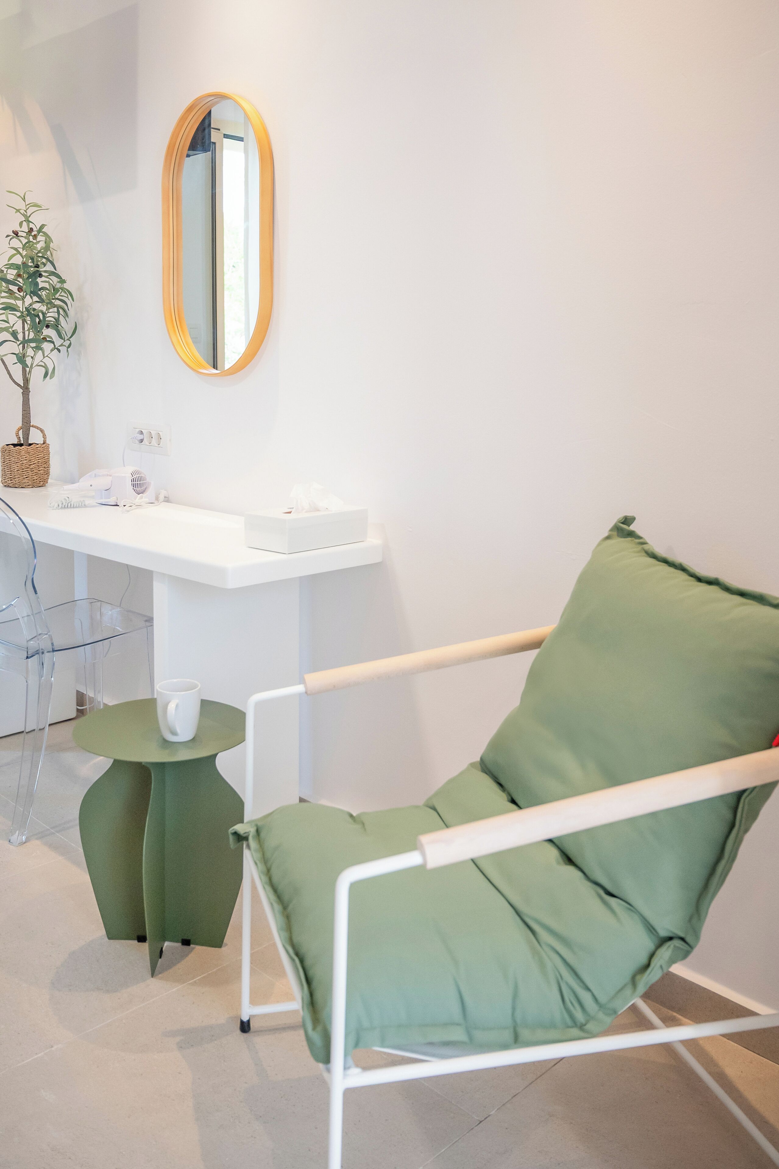 Una habitación con un escritorio blanco, una silla verde, una mesita redonda y un espejo en la pared.