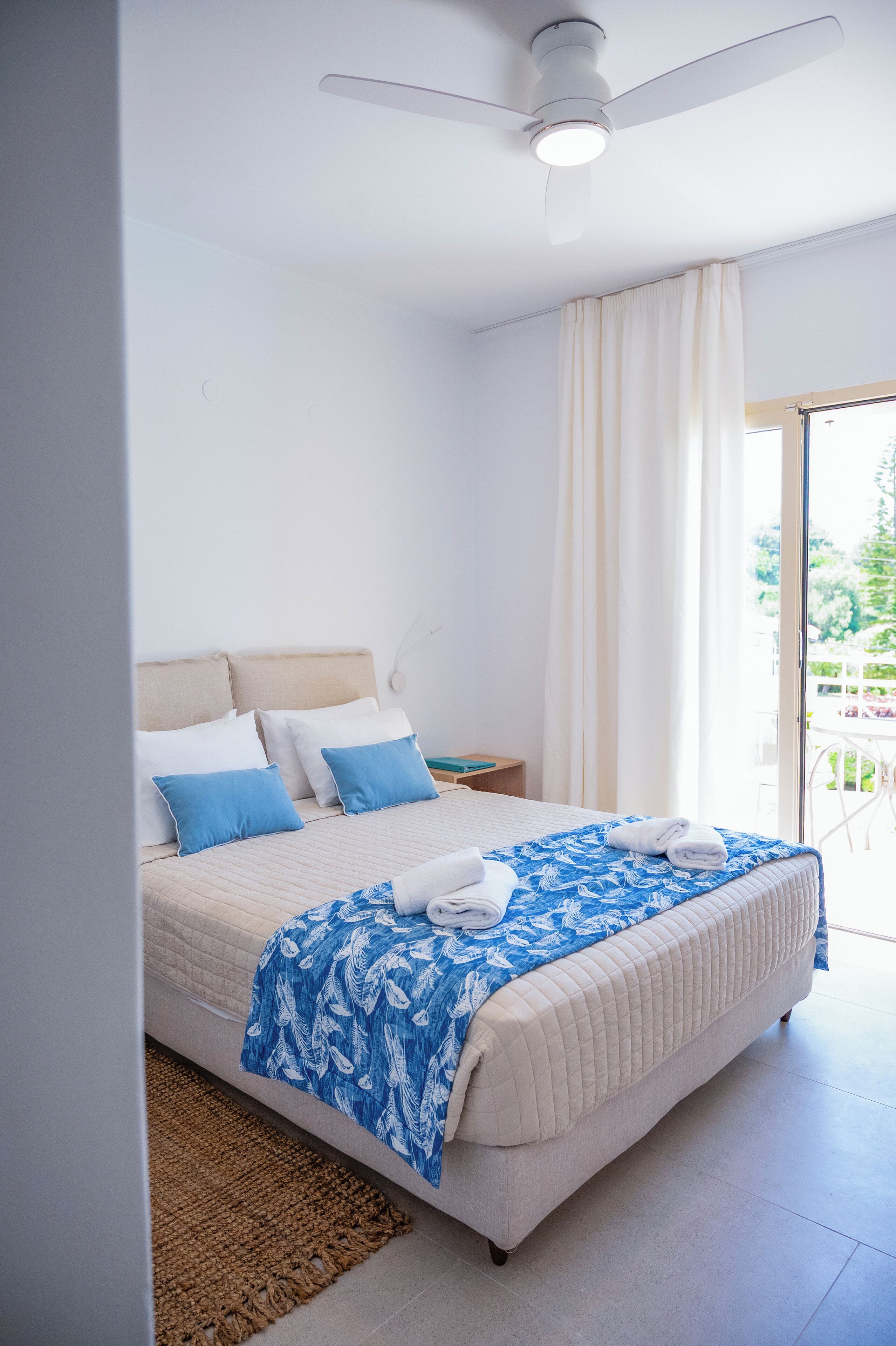 A bedroom with a bed, a ceiling fan, a nightstand, and a view of the outdoors.