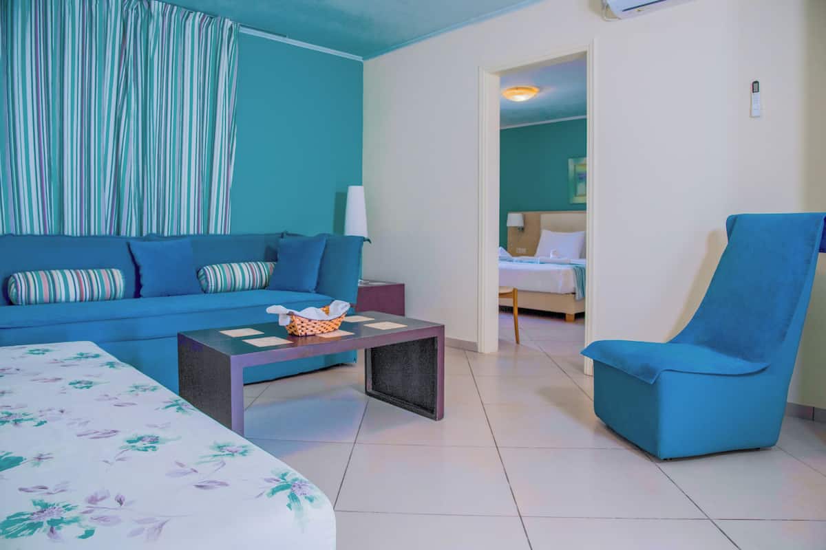 A room with a blue sofa, a blue armchair, a small table, and a bed in the background.
