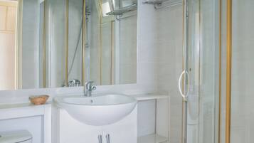 A modern bathroom with a white sink, a glass shower enclosure, and a large mirror.