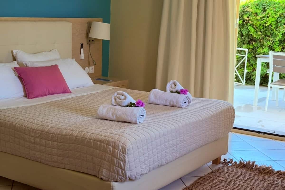 A neatly made bed with a beige quilt, two pillows, and two rolled towels with flowers.