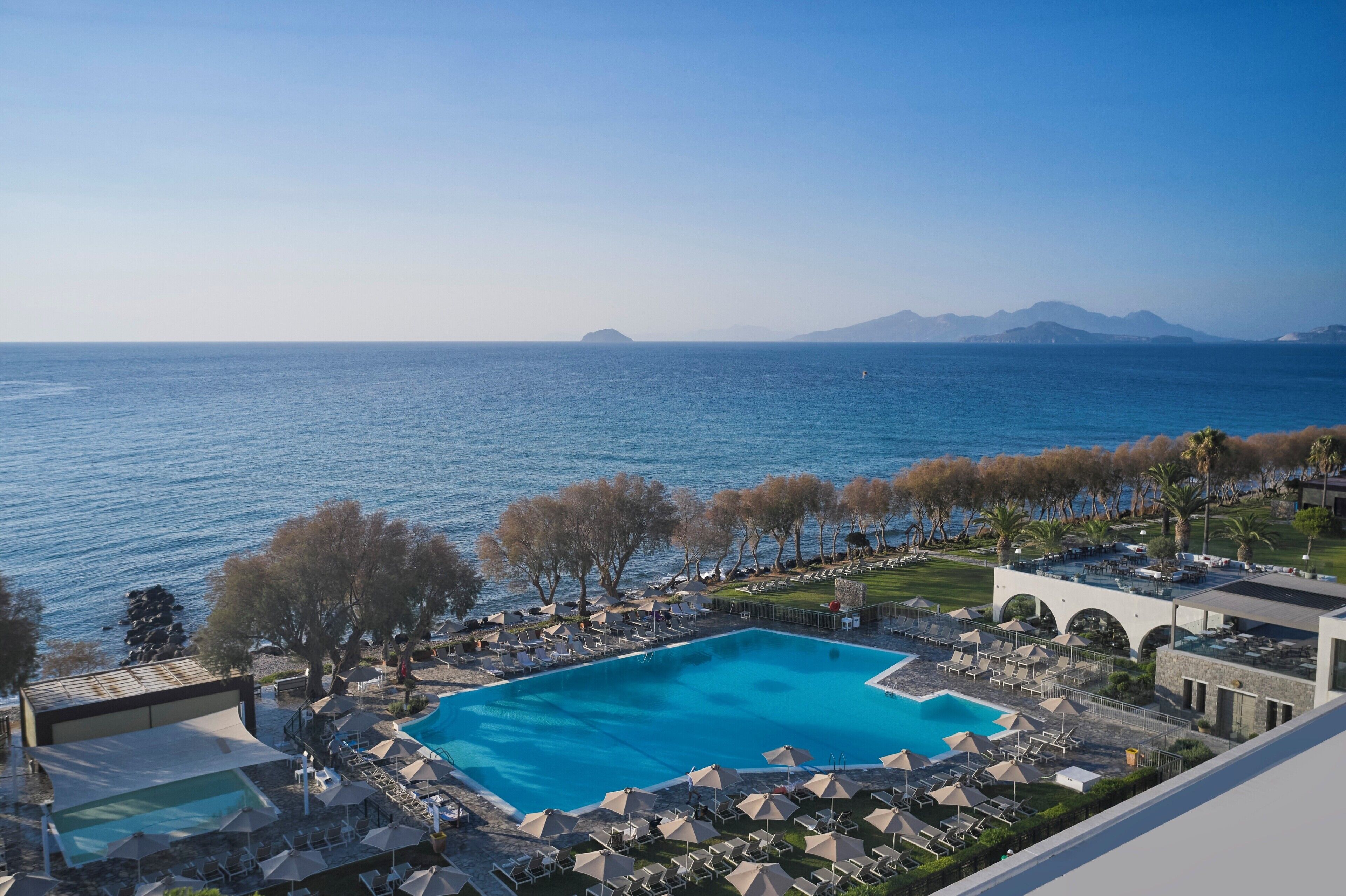 Un resort con piscina, sillas de descanso, sombrillas y vistas al mar.