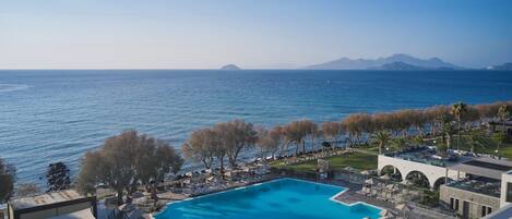 A resort with a pool, lounge chairs, umbrellas, and a view of the sea.