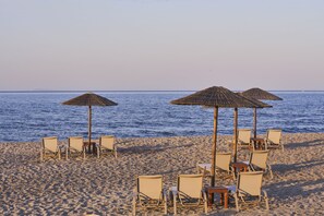 Une plage bordée de rangées de chaises longues et d’ombrelles en chaume, donnant sur la mer.