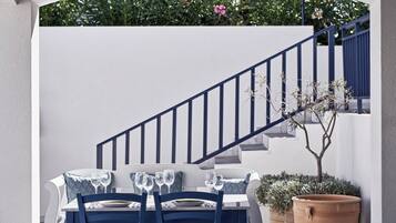 Comedor con mesa dispuesta para dos, una escalera y vista a un jardín con flores.