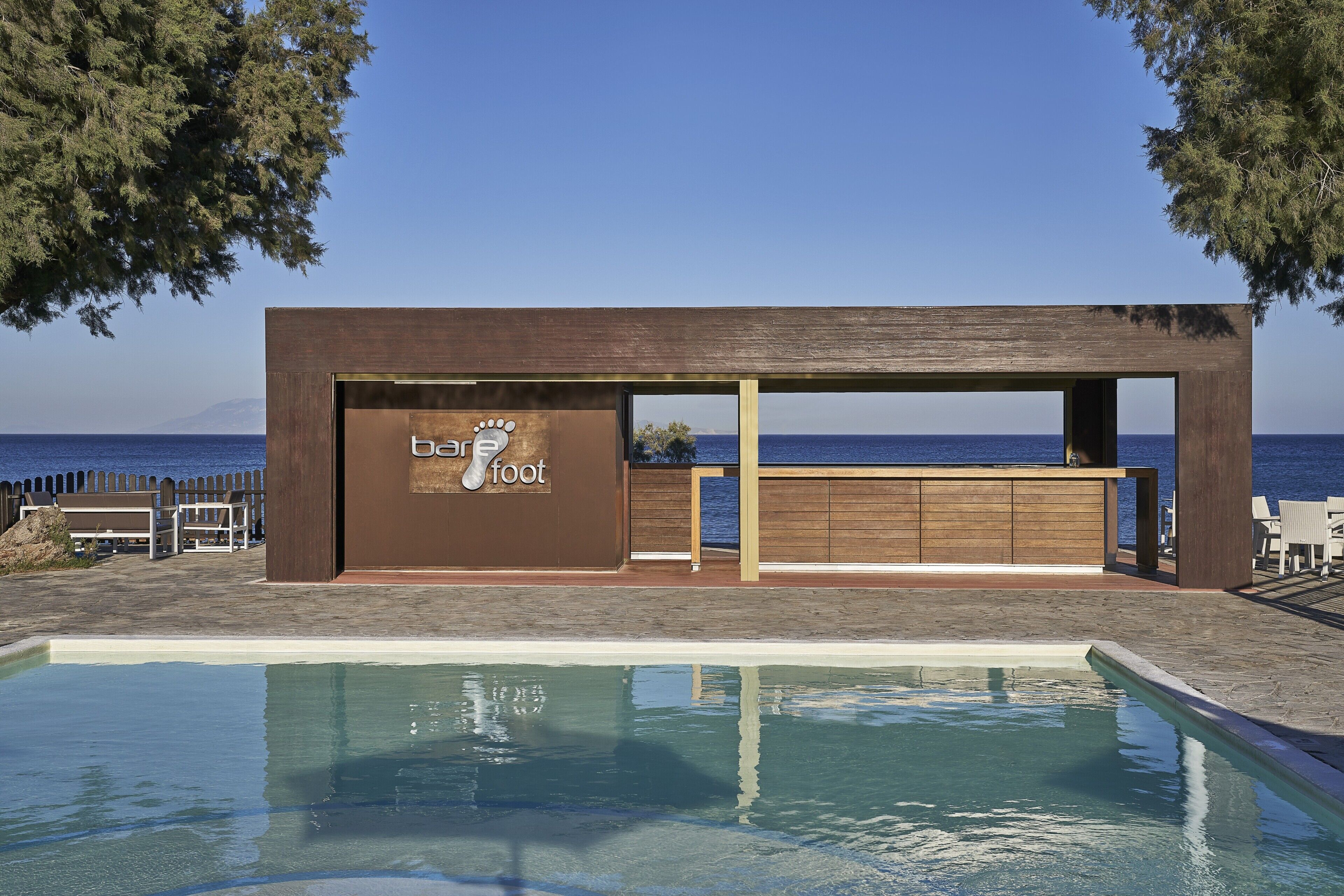 Um bar à beira da piscina com vista para o mar, um deck de madeira e céu claro.