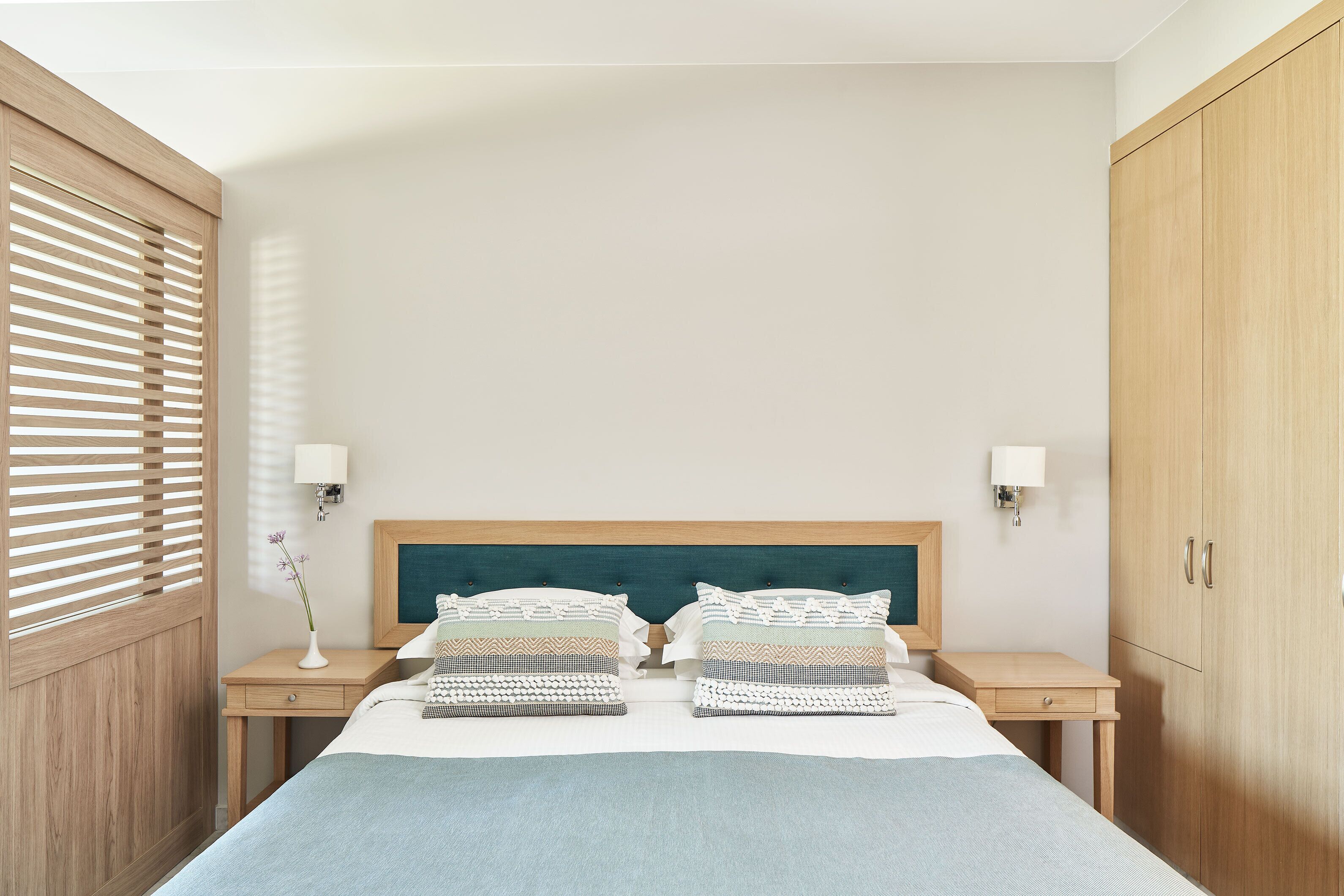 A bedroom with a bed, two bedside tables, a nightstand, a lamp, a wall-mounted light, and a wardrobe.