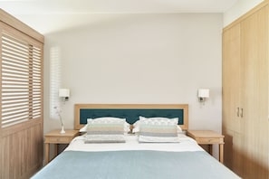 Une chambre à coucher comprenant un lit, deux tables de chevet, une commode, une lampe, un luminaire fixé au mur et une armoire.