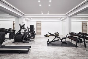 Ein modernes Fitnessstudio mit Laufbändern, Crosstrainern, einer Gewichtbank und Kurzhanteln.