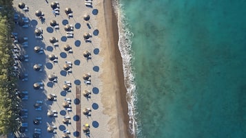 Vista aérea de una playa con filas de tumbonas y sombrillas, un paseo de madera y agua turquesa cristalina.