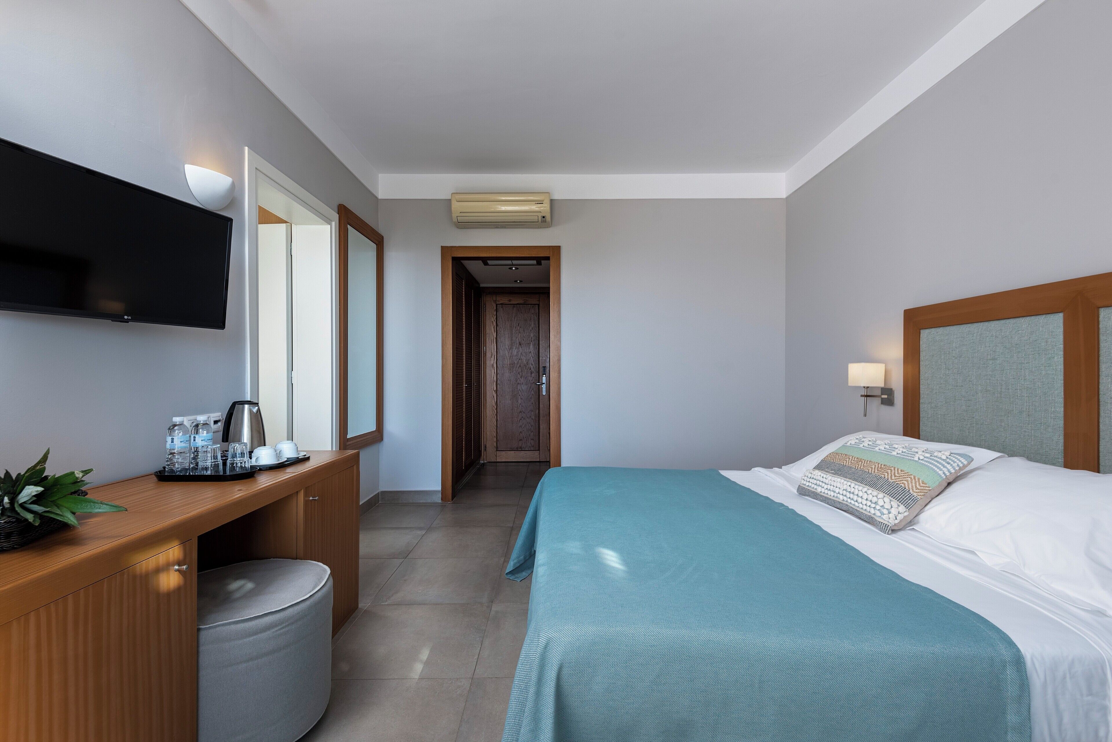 A hotel room with a bed, a desk with a flat-screen TV, a coffee maker, and a plant.