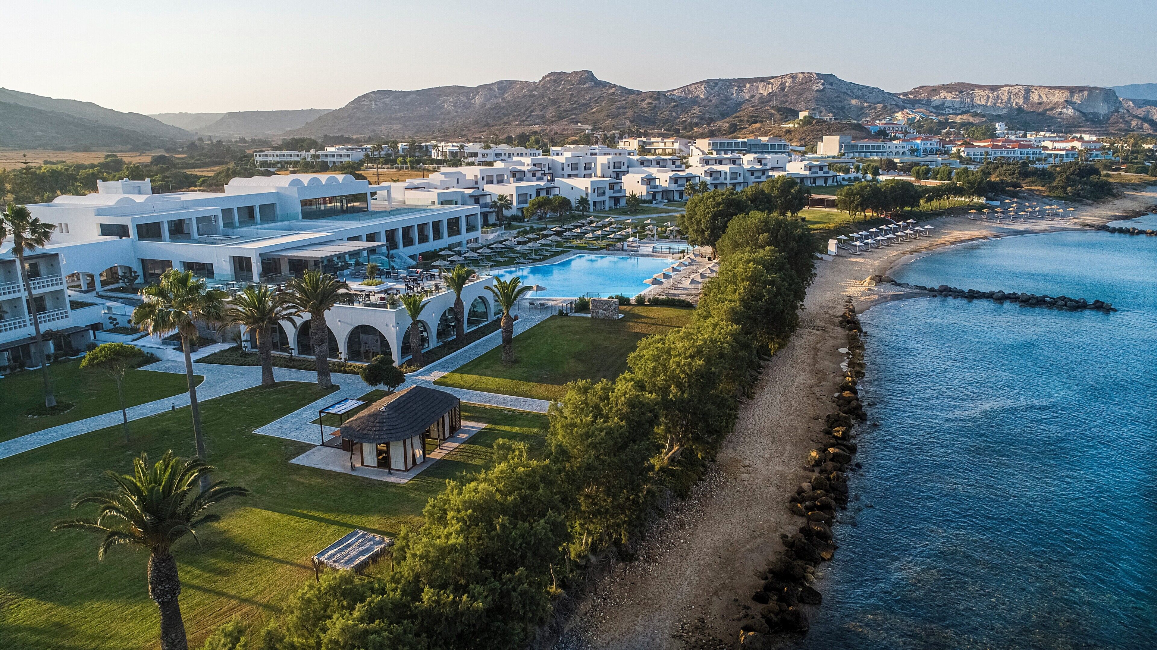 Un resort con piscina, playa y montañas al fondo.