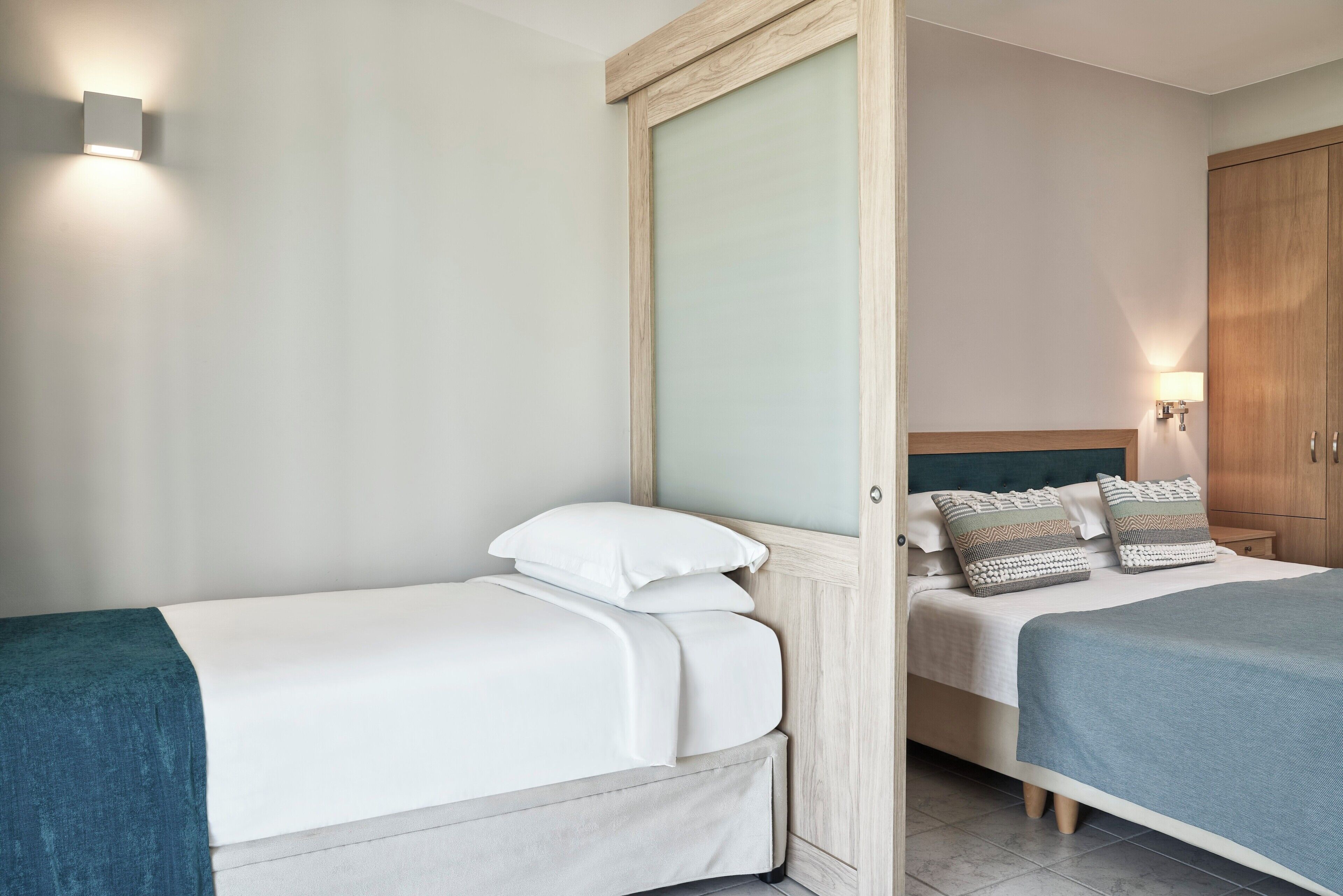 Una habitación de hotel con dos camas, un armario de madera y una mesita de noche con lámpara.